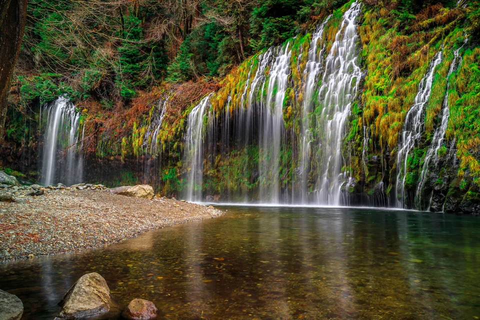 water cascading over a moss-covered rock wall into a clear pool